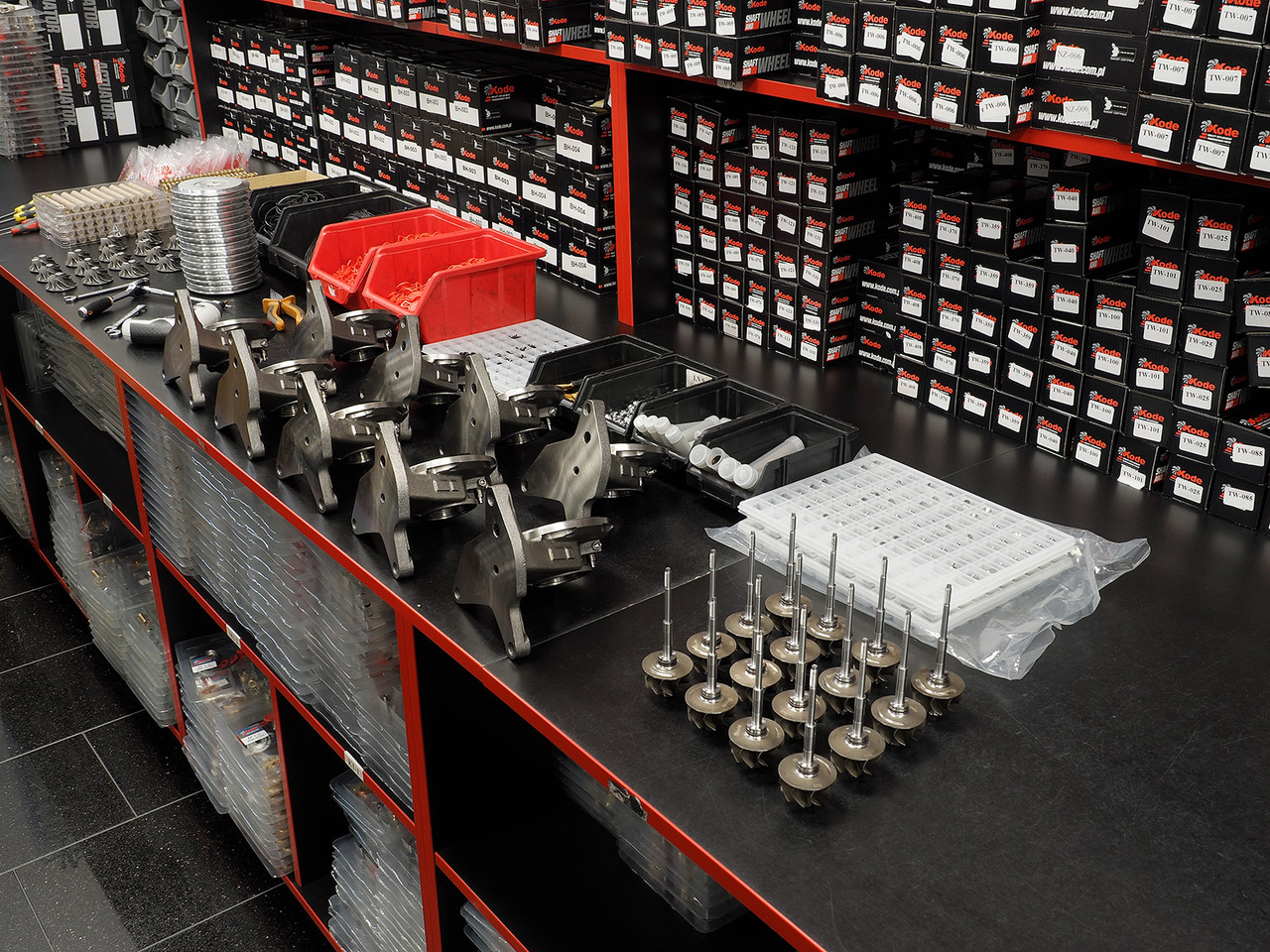 Brake components warehouse with calipers, drums, and wheel parts arranged on a black and red counter, with rows of parts boxes on the walls