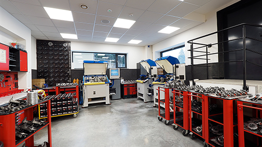 Interior of a professional turbocharger repair workshop showing organized workstations with red tool cabinets, specialized equipment, and various turbocharger parts on display